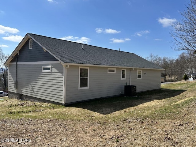 rear view of house with a shingled roof, central AC unit, and a yard