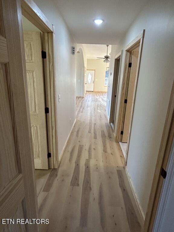 hallway with light wood-style flooring, baseboards, arched walkways, and recessed lighting