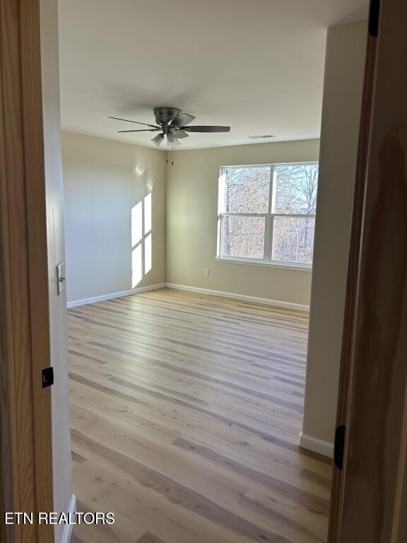 empty room with light wood-style flooring, baseboards, a ceiling fan, and visible vents