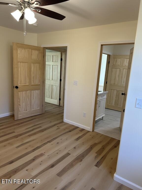 unfurnished bedroom featuring ensuite bathroom, light wood-style flooring, baseboards, and ceiling fan