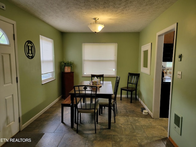 dining area featuring a textured ceiling, baseboards, stone finish flooring, and visible vents