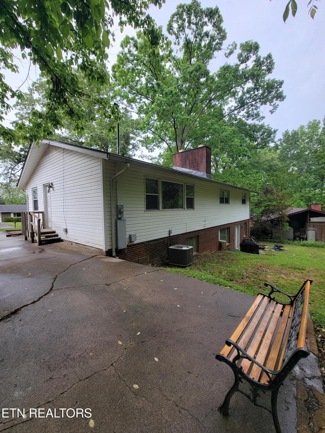back of property featuring central air condition unit, a yard, a chimney, and entry steps