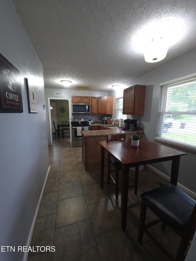 kitchen featuring a sink, a peninsula, a textured ceiling, dark tile patterned floors, and appliances with stainless steel finishes