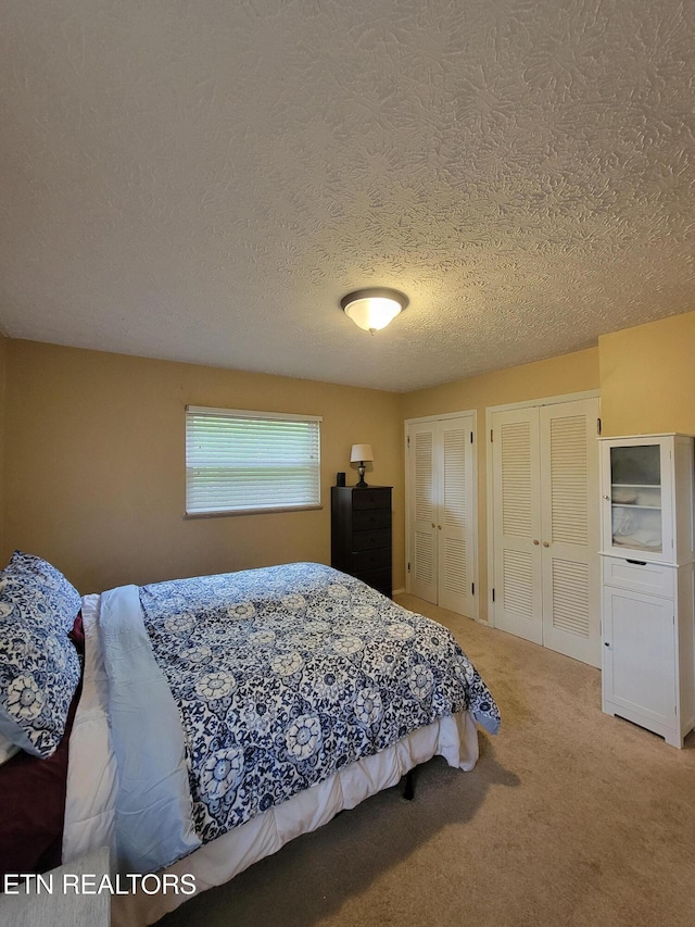 bedroom with two closets, light carpet, and a textured ceiling