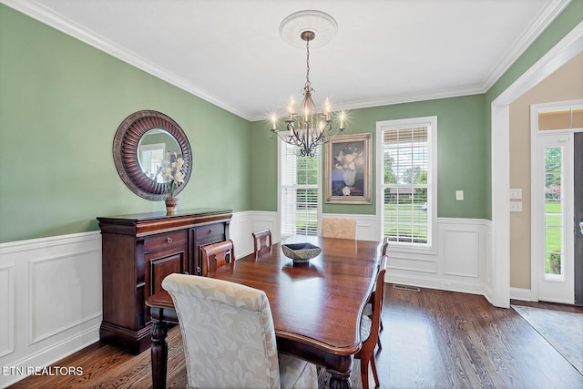 dining room featuring a chandelier, dark wood finished floors, wainscoting, ornamental molding, and a decorative wall