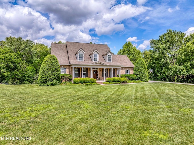 new england style home with covered porch, a front yard, and brick siding