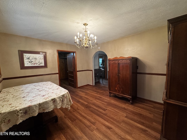 dining room with an inviting chandelier, dark wood finished floors, a textured ceiling, baseboards, and arched walkways