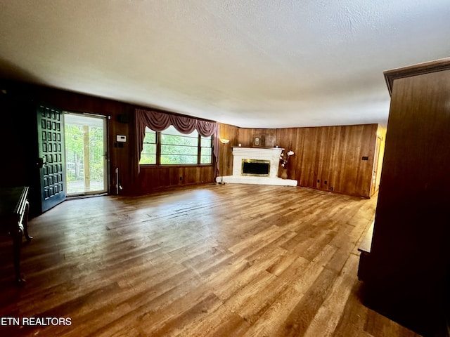 unfurnished living room featuring wooden walls, a fireplace with raised hearth, and wood finished floors