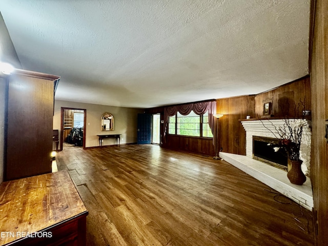 unfurnished living room with wood finished floors, a brick fireplace, a textured ceiling, wood walls, and baseboards