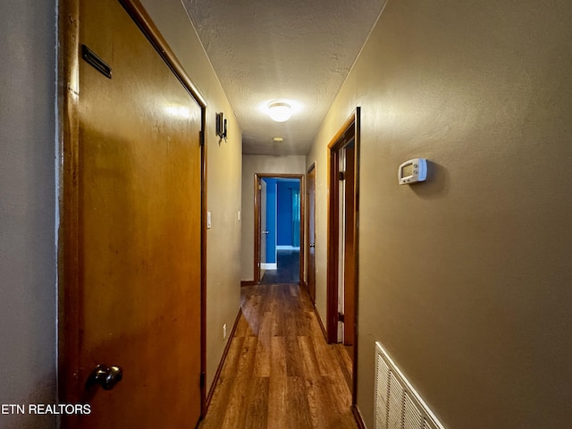 hall with a textured ceiling, baseboards, visible vents, and wood finished floors