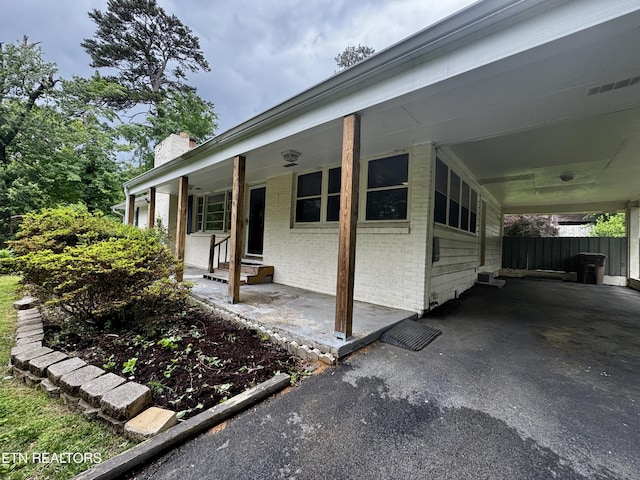 view of side of property featuring a chimney, fence, a carport, brick siding, and entry steps