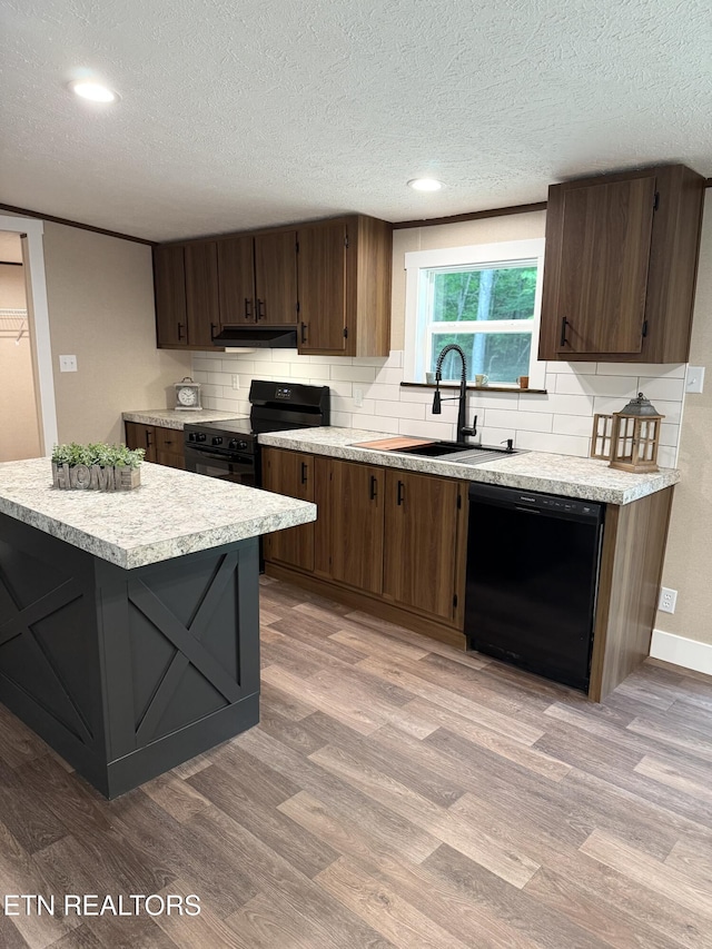 kitchen with under cabinet range hood, a sink, black appliances, light countertops, and light wood-type flooring