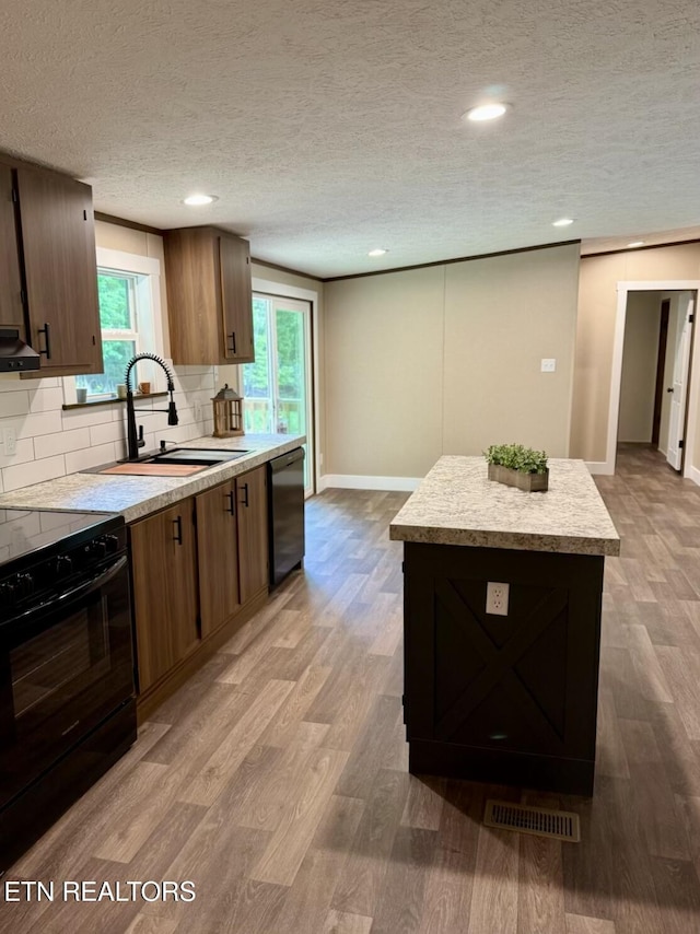 kitchen featuring dishwashing machine, a sink, black range with electric cooktop, light countertops, and a kitchen island