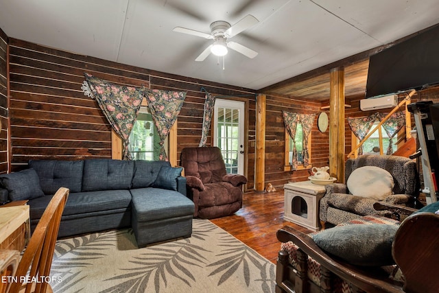 living room with wooden walls, wood finished floors, a ceiling fan, and a wall mounted air conditioner