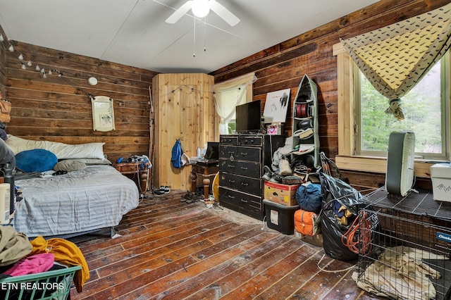 bedroom featuring hardwood / wood-style flooring, wood walls, and ceiling fan
