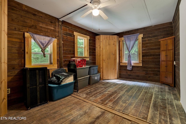 unfurnished room with wood-type flooring, wood walls, and a ceiling fan