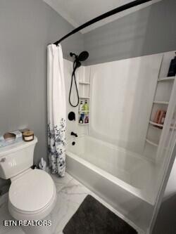 bathroom featuring toilet, marble finish floor, and shower / bath combo with shower curtain