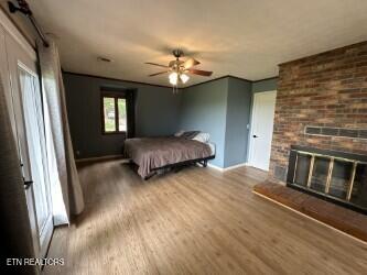 bedroom featuring a ceiling fan, wood finished floors, baseboards, and a brick fireplace