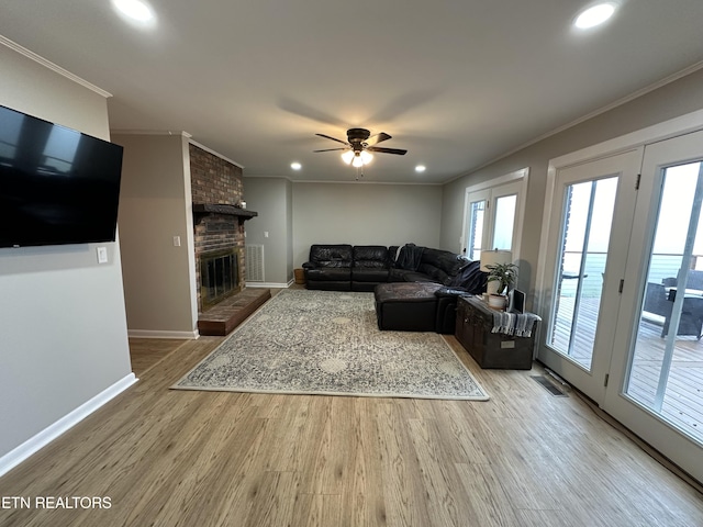 living room featuring light wood-type flooring, visible vents, crown molding, a brick fireplace, and a ceiling fan