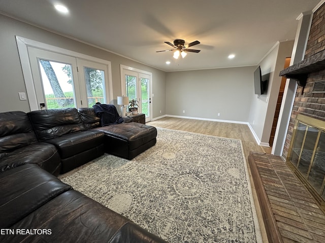 living room featuring ornamental molding, light wood-style floors, a ceiling fan, and a brick fireplace