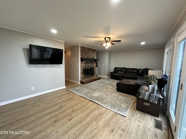 living room with wood finished floors, a ceiling fan, a fireplace, visible vents, and baseboards
