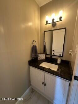 bathroom featuring marble finish floor, baseboards, vanity, and lofted ceiling