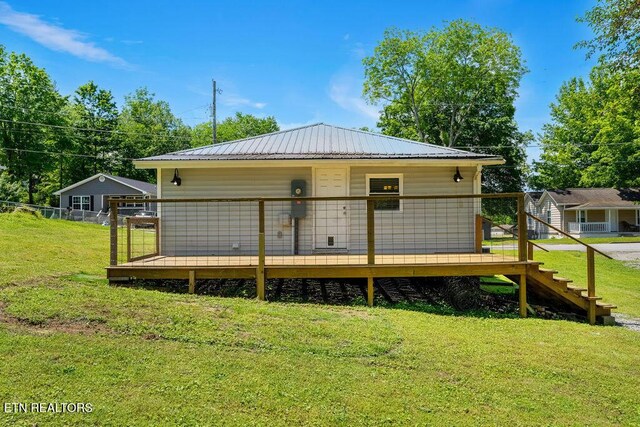 back of property with a yard, metal roof, a wooden deck, and stairway