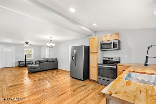 kitchen with light brown cabinetry, butcher block countertops, light wood finished floors, a sink, and stainless steel appliances