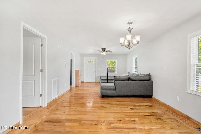 living area featuring light wood finished floors, visible vents, baseboards, and ceiling fan with notable chandelier
