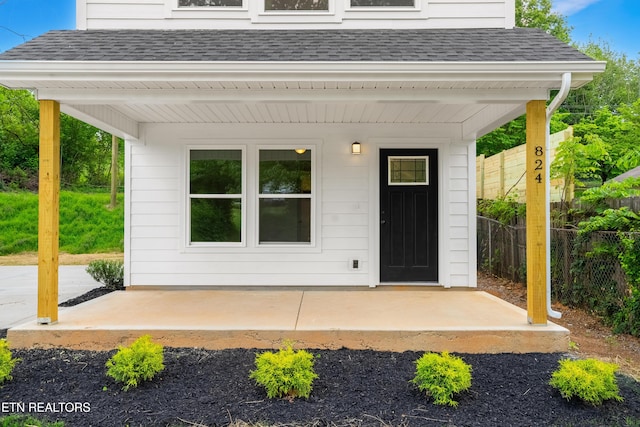 property entrance with a shingled roof, a patio area, and fence