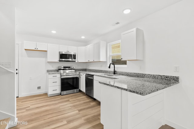 kitchen with a peninsula, a sink, stainless steel appliances, light wood-type flooring, and light stone countertops
