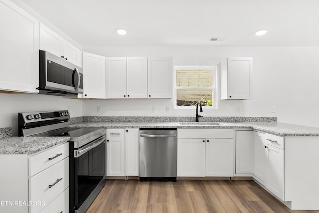 kitchen with a sink, white cabinets, appliances with stainless steel finishes, light stone counters, and recessed lighting