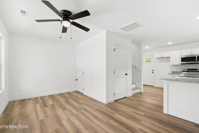 unfurnished living room featuring ceiling fan, stairs, light wood-type flooring, and visible vents