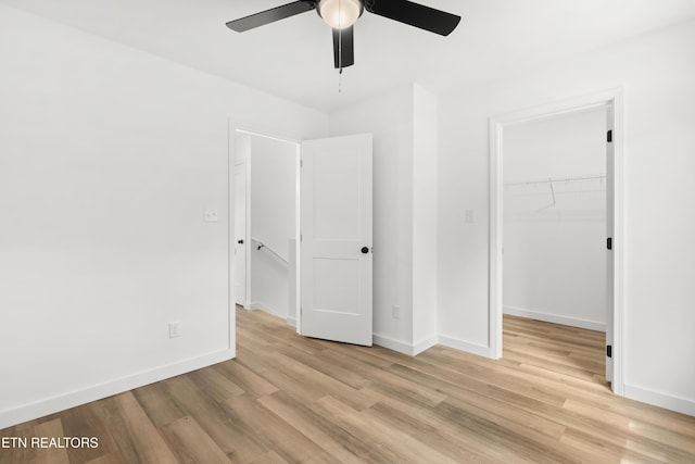 unfurnished bedroom with baseboards, a spacious closet, light wood finished floors, and a closet