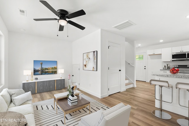 living room featuring stairway, light wood finished floors, and visible vents