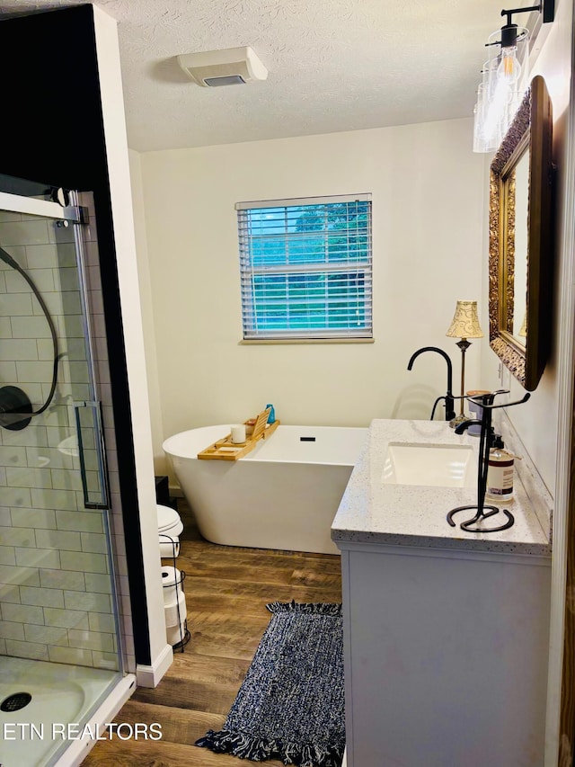 full bathroom with a stall shower, vanity, a freestanding bath, and wood finished floors