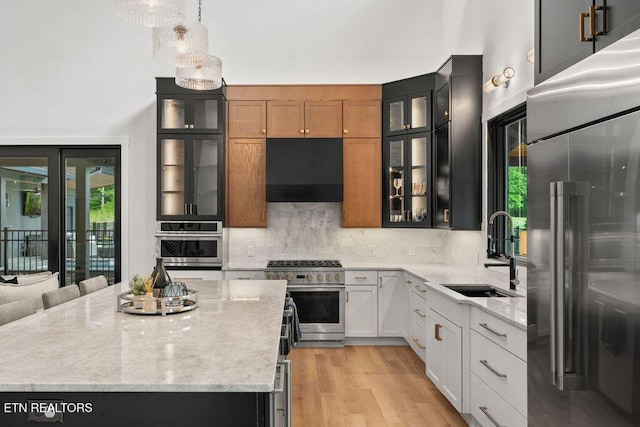 kitchen featuring a sink, high end appliances, extractor fan, backsplash, and light stone counters