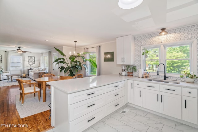 kitchen featuring a sink, a peninsula, white cabinetry, open floor plan, and light countertops