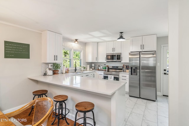 kitchen featuring a peninsula, a breakfast bar area, a sink, stainless steel appliances, and marble finish floor