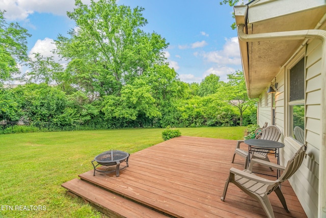 wooden terrace featuring an outdoor fire pit, a lawn, and view of wooded area
