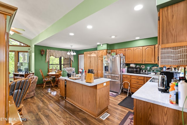 kitchen featuring stainless steel fridge with ice dispenser, a center island, light countertops, wood finished floors, and a ceiling fan