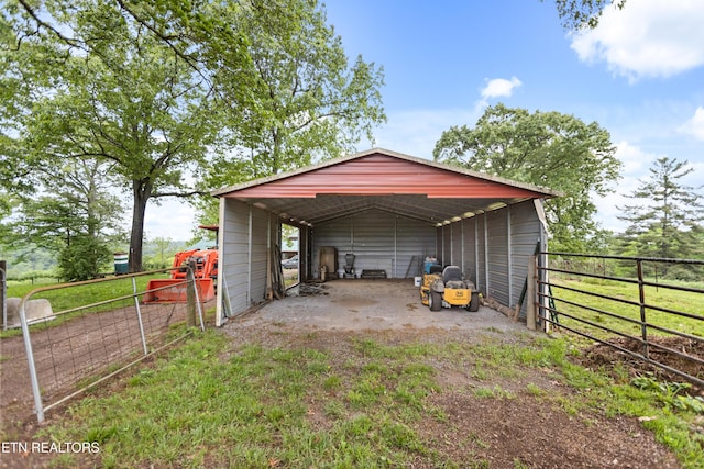 view of outdoor structure with a carport, an outbuilding, driveway, and fence