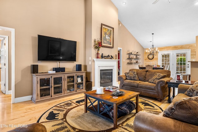 living area with light wood-style floors, high vaulted ceiling, a chandelier, a glass covered fireplace, and baseboards