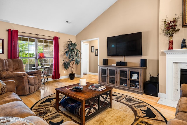 living room featuring high vaulted ceiling, light wood-type flooring, baseboards, and a fireplace