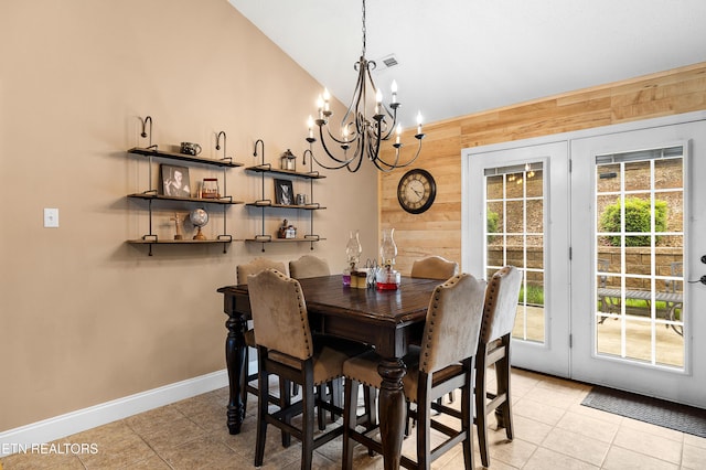 dining room with wood walls, a chandelier, lofted ceiling, light tile patterned flooring, and baseboards