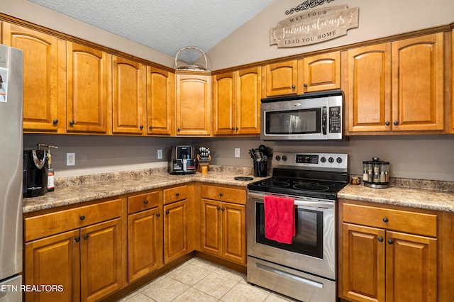 kitchen with stainless steel appliances, light tile patterned floors, brown cabinets, light countertops, and a textured ceiling