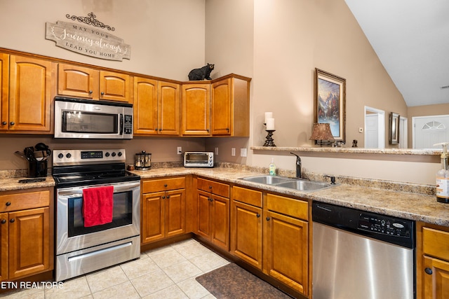 kitchen with appliances with stainless steel finishes, a sink, light tile patterned flooring, high vaulted ceiling, and brown cabinets