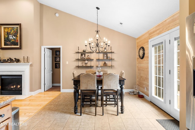 dining space with a chandelier, light tile patterned floors, wooden walls, high vaulted ceiling, and baseboards