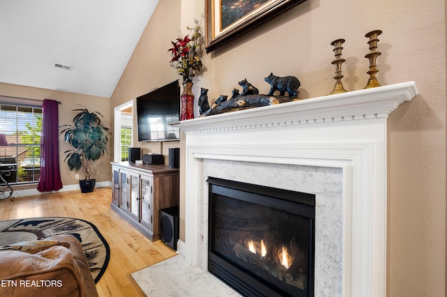 living area with a premium fireplace, light wood-style floors, high vaulted ceiling, and baseboards
