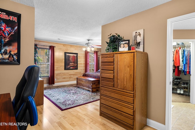 home office with wood walls, a textured ceiling, ceiling fan, light wood finished floors, and baseboards